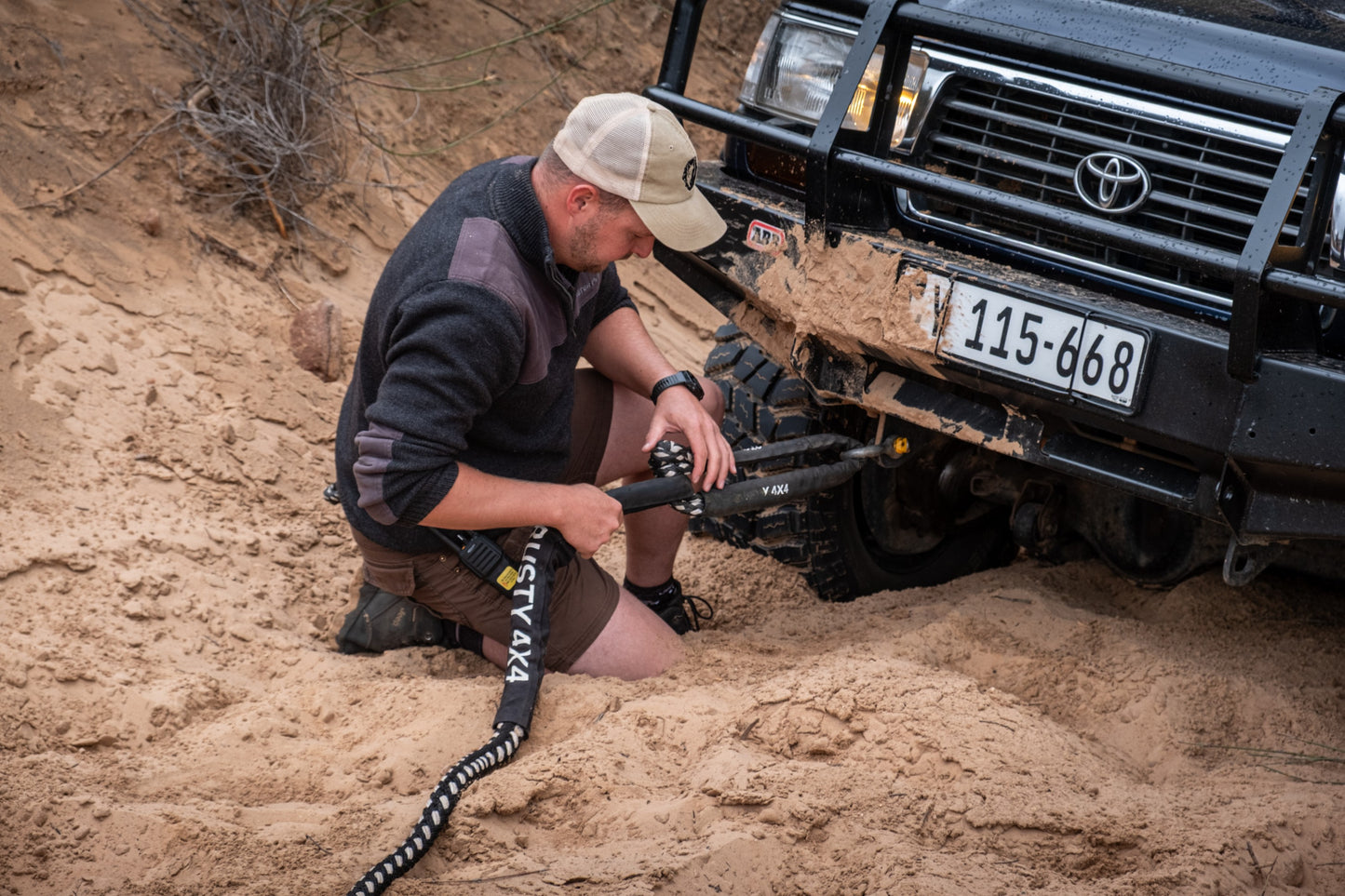 Kinetic recovery strap and chain in sand beside an off-road truck