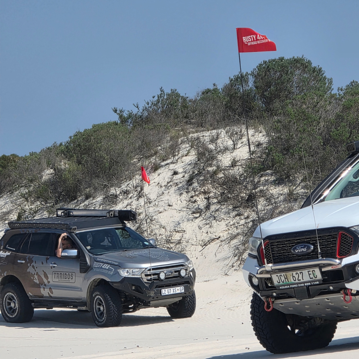 Red 4x4 dune safety flag on vehicle whip, shown on two off-road vehicles