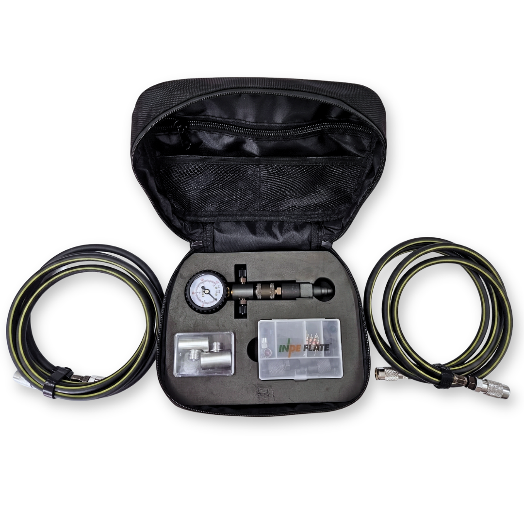 A black zippered carrying case opened to display a tire pressure gauge kit with two coiled black and green air hoses, a gauge, and small accessory compartments on a white background.