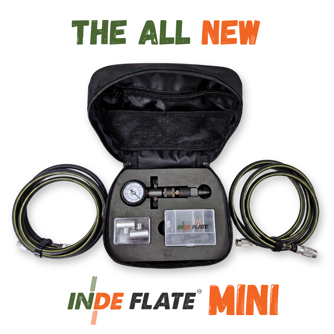 An open black zippered carrying case displaying an inflatable repair kit with a gauge, metal fittings, and two coiled green-and-black hoses on a white background, with 'THE ALL NEW INDE FLATE MINI' text above and below.