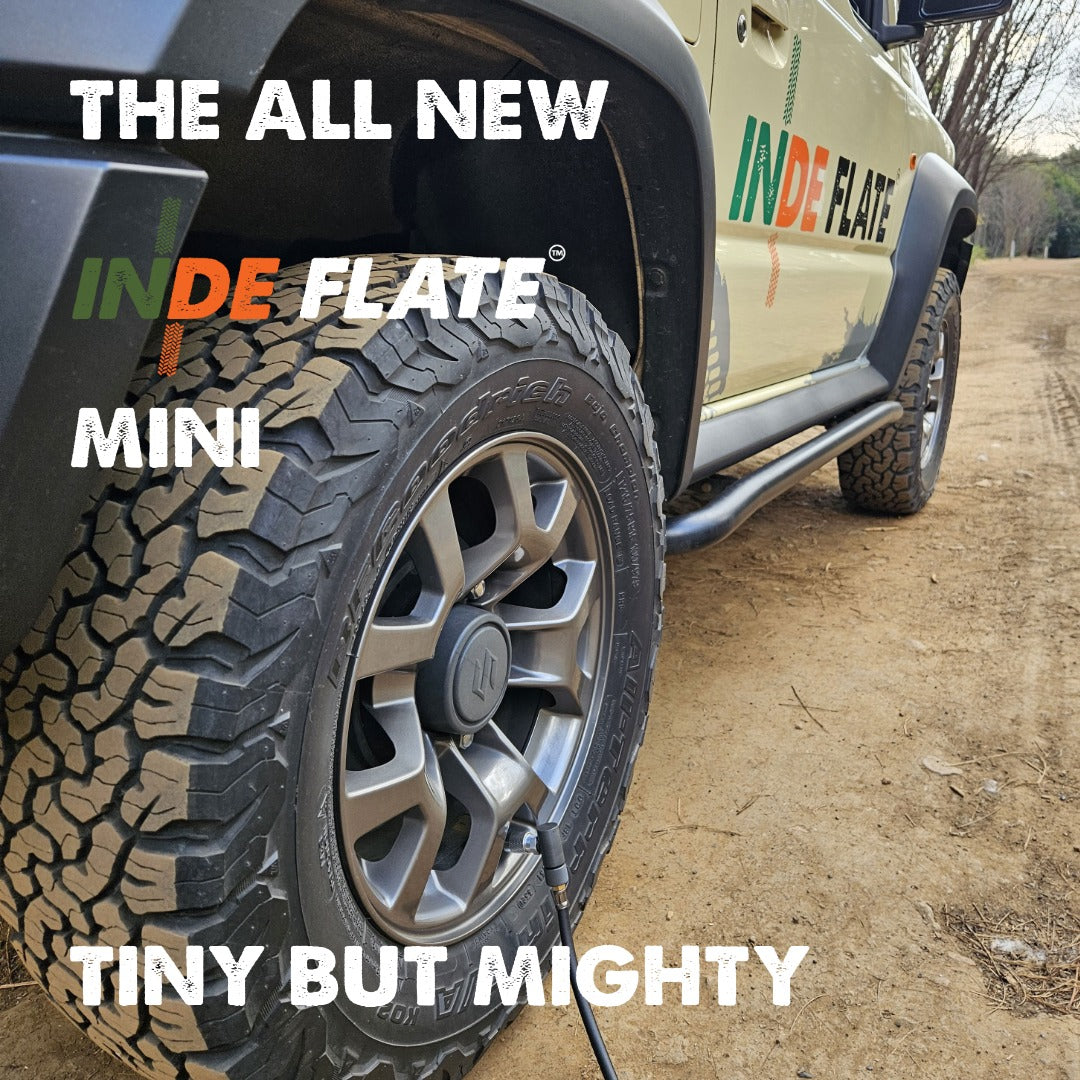 A close-up outdoor shot of a vehicle tire with a visible valve stem and pump nozzle, overlaid with large text reading 'THE ALL NEW INDEFLATE MINI' and 'TINY BUT MIGHTY.' The vehicle body also shows the INDEFLATE logo.